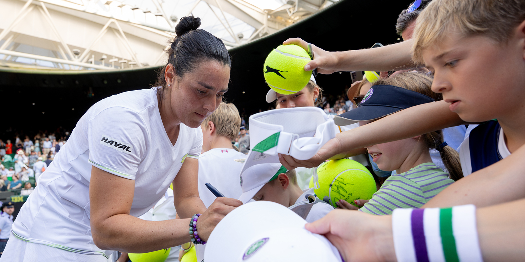 Women's tennis player Ons Jabeur singing fan autographs on Centre Court at Wimbledon in 2023 after a tennis match