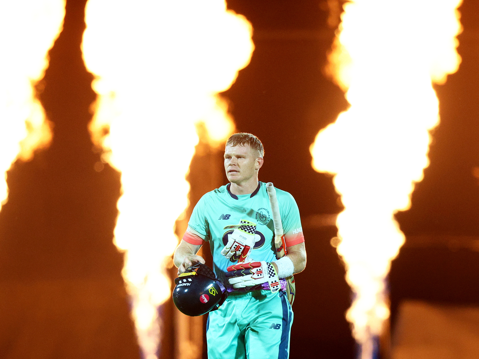 Oval Invincibles men's cricket player walking out for a match in The Hundred tournament with fire behind him