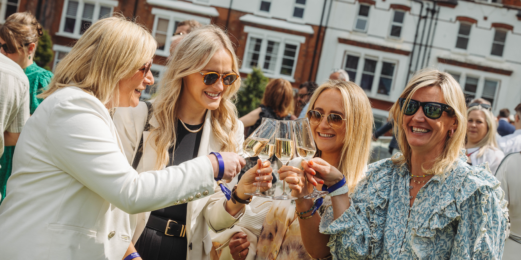 Guests holding their glasses of Champagne to cheers while smiling on the Roof Garden Balcony at The Queen's Club