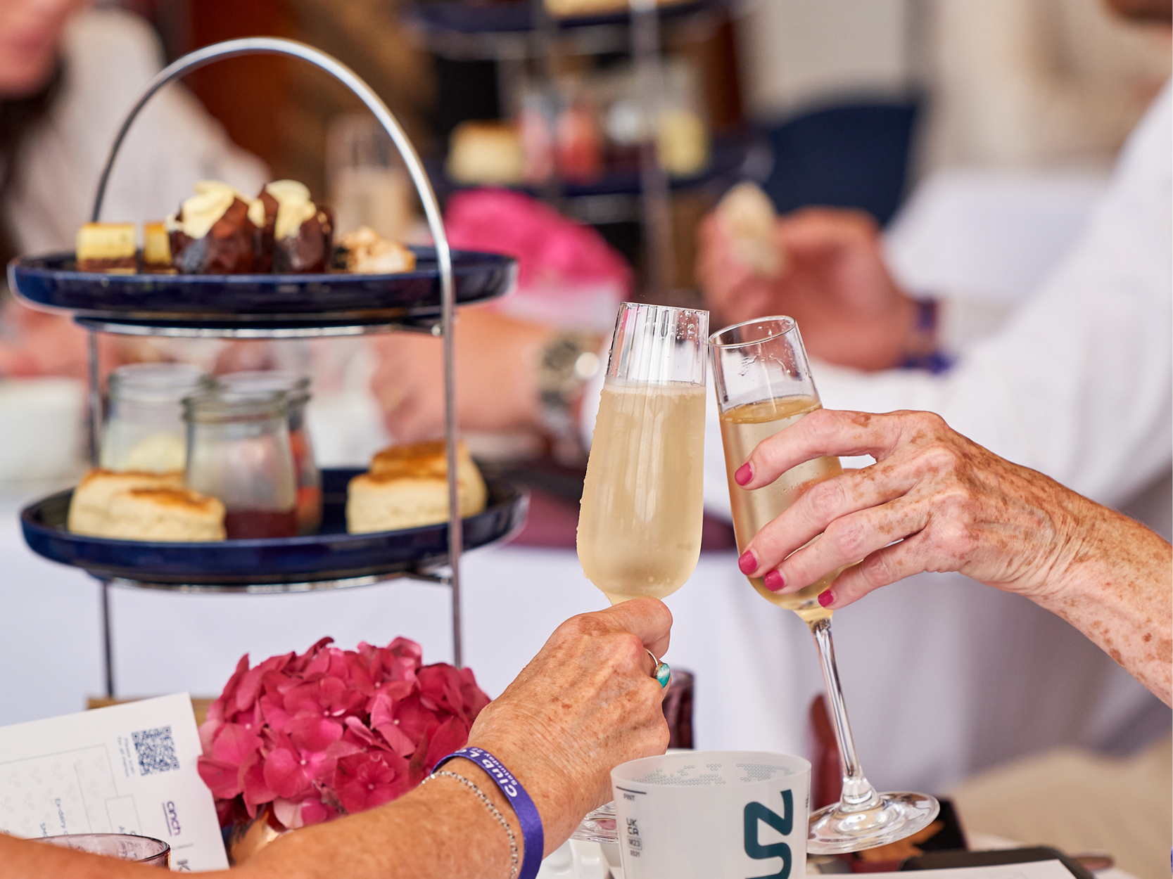 Guests holding glasses Champagne making a cheers while enjoying afternoon tea at Club lounge hospitality at The Queen's Club Championships 2024