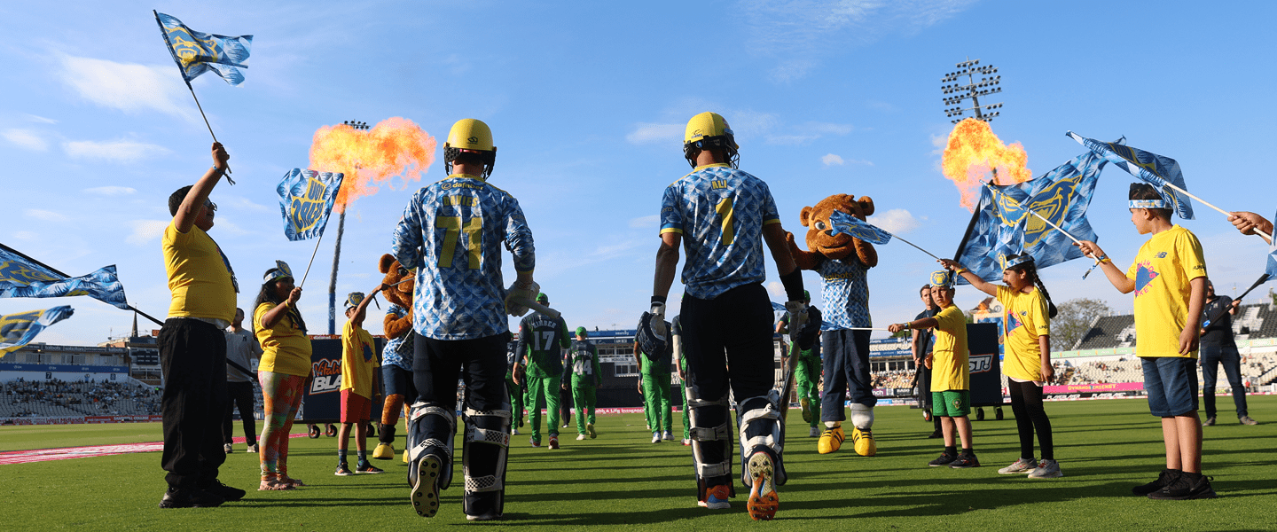 Two Birmingham Bears T20 cricket players walking onto the pitch with fireworks before a match at Edgbaston Stadium 