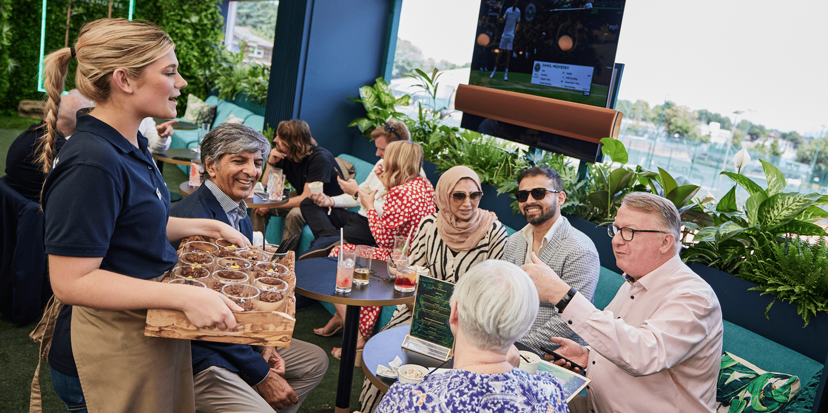 Waiting staff in the Treehouse hospitality area at Wimbledon talking to guests at their seats serving food dishes