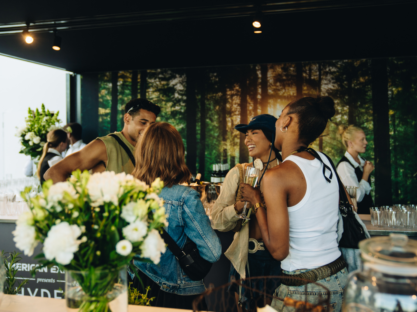 Group of friends chatting and laughing by the bar in the Great Oak Roof Garden hospitality at BST Hyde Park