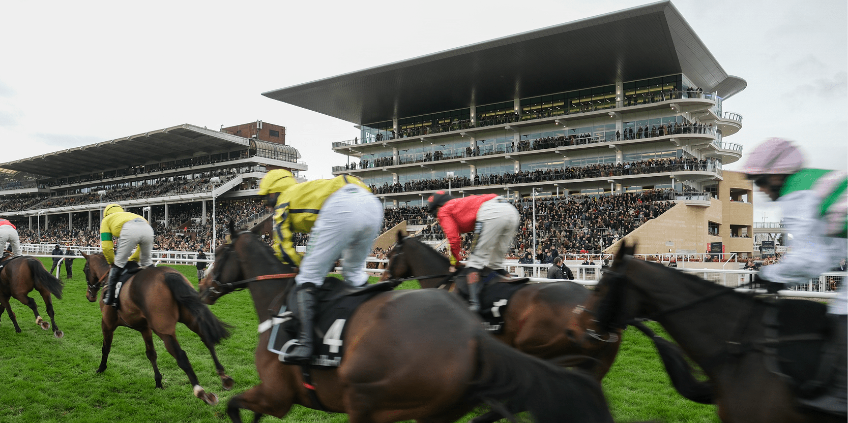 Cheltenham Racecourse grandstand with horses and jockeys racing during the Cheltenham horse racing Festival