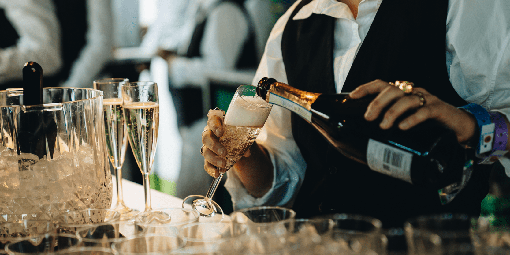 Waitress pouring a glass of Champagne behind the bar in the Great Oak Roof Garden hospitality at BST Hyde Park