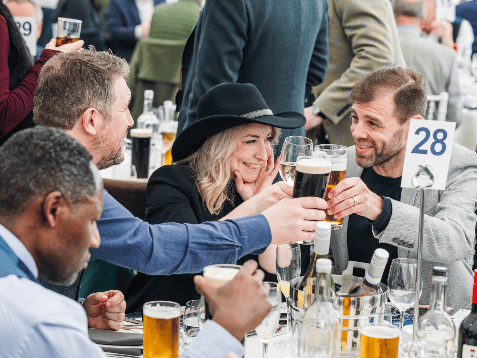 A group of friends smiling and clinking glasses at a table in hospitality at Cheltenham Festival