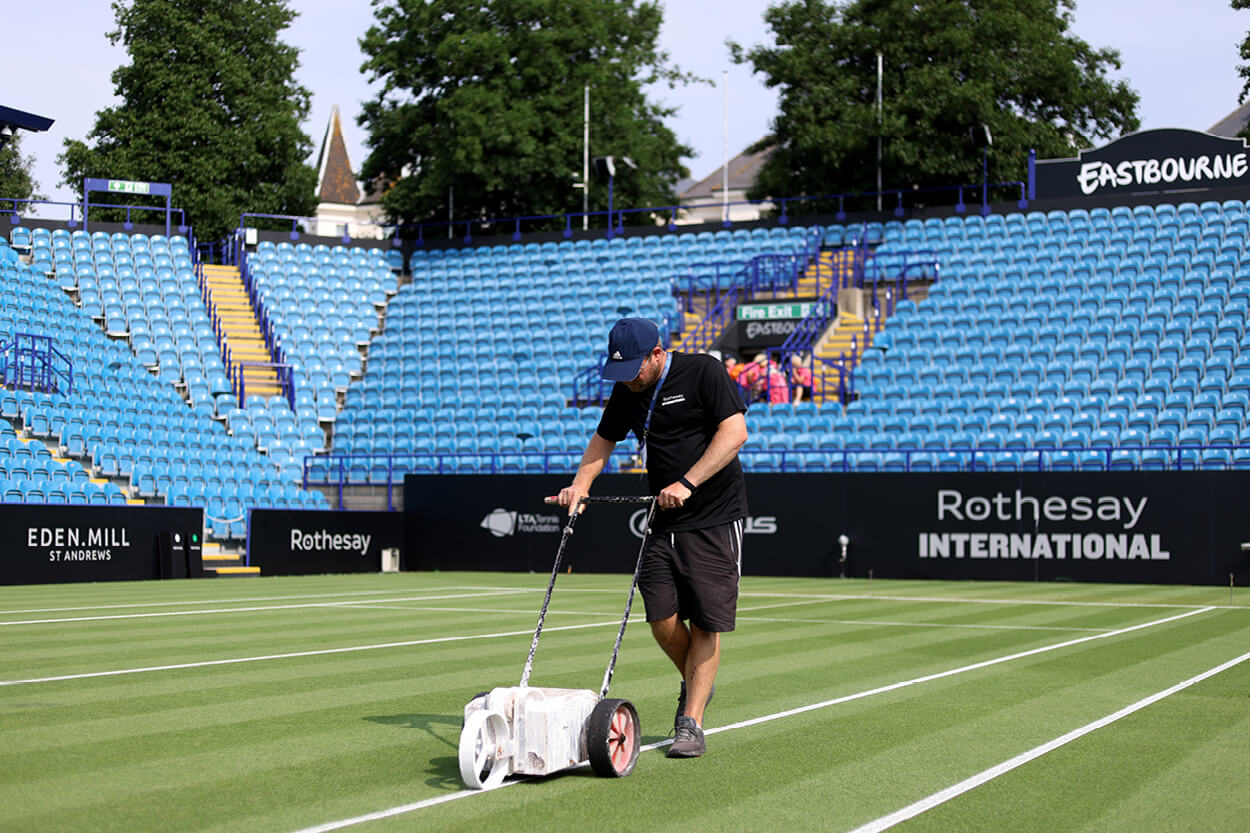 Groundsman marking the white lines on a grass tennis court at Eastbourne international tennis tournament before a tennis match
