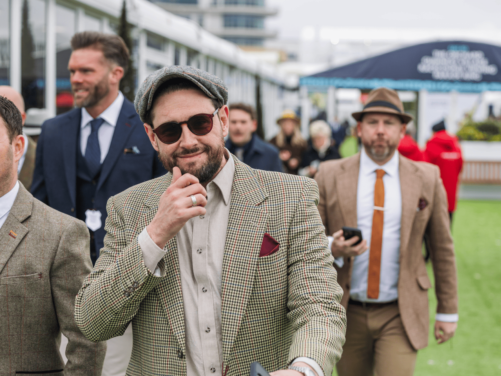 A man smiling at the camera dressed in Tweed jacket walking into Cheltenham Festival