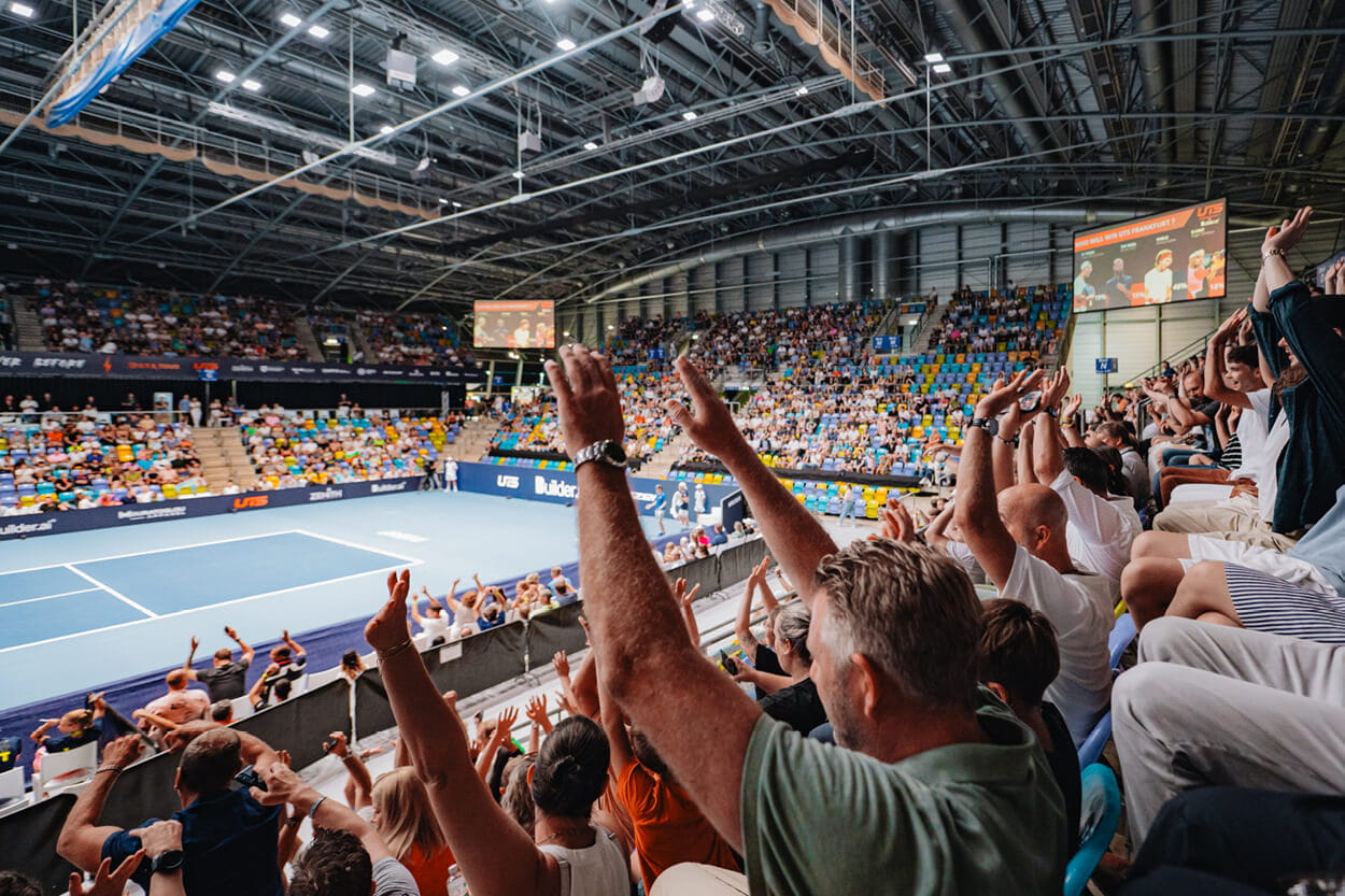 View of the tennis court at UTS tennis tournament from the crowd seats with fans hands in the air