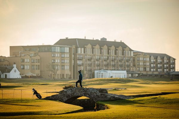 Golfer posing for a photo on the Swilcan Bridge at Dusk, in St Andrews, Scotland.
