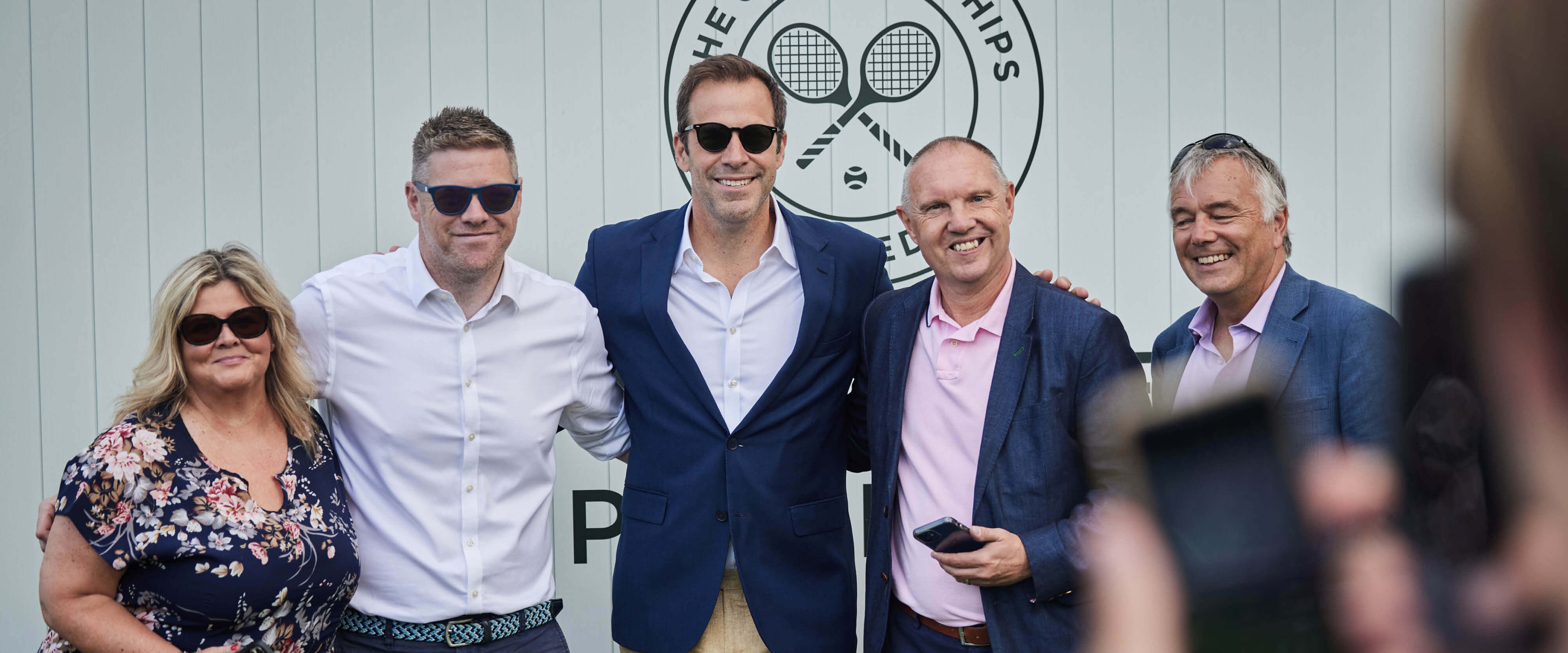 Former British number one tennis player Greg Rusedski smiling in a group photo with guests in Rosewater Pavilion hospitality facility at The Championships Wimbledon