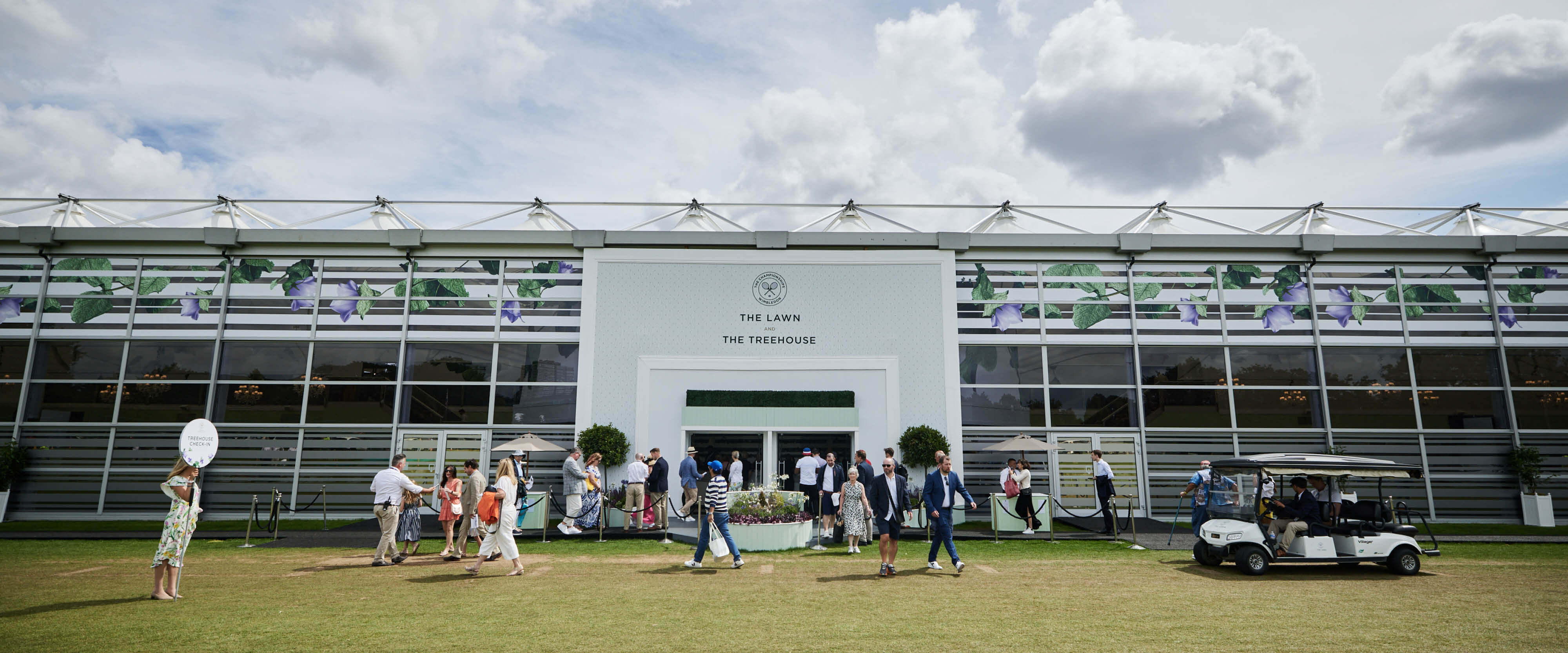 Outside view of The Lawn hospitality facility with guests entering and golf buggies taking guests to court at The Championships Wimbledon